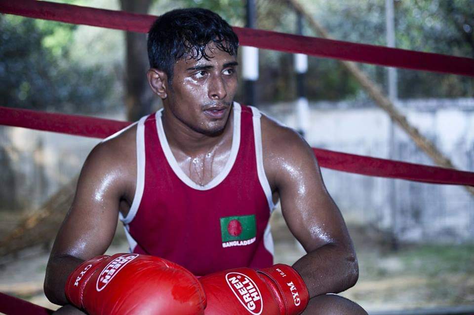 Al-Amin in a red Bangladesh vest and red gloves, resting in the ring corner