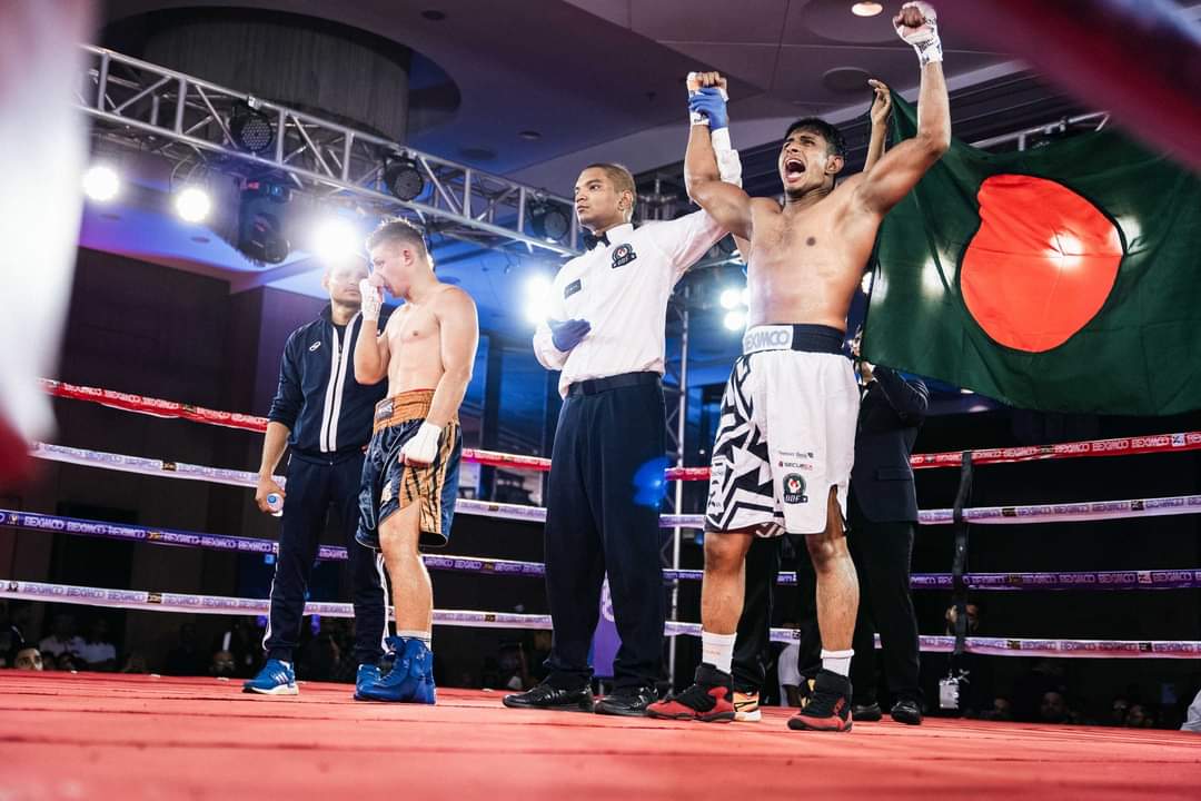 The referee raises Al-Amin's hand, the Bangladesh flag behind the ring
