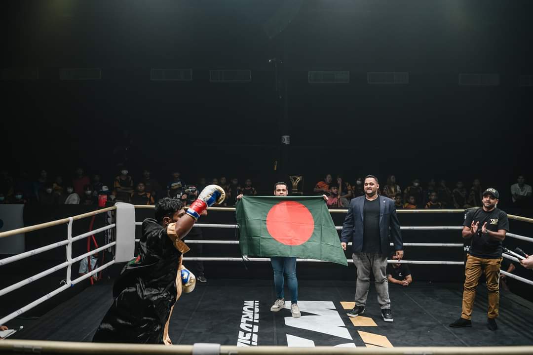 Al-Amin raising a glove in the ring as the Bangladesh flag is held up