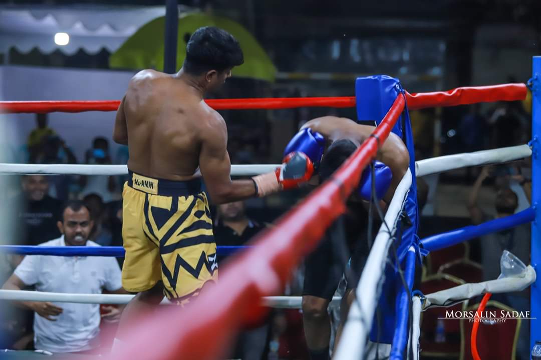 A boxer in yellow and black shorts working an opponent on the ropes