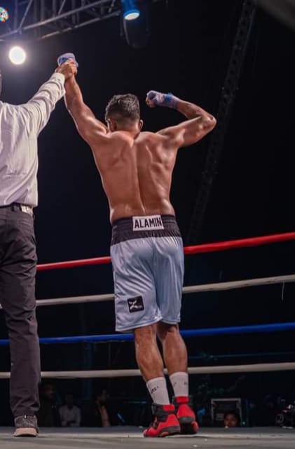 Al-Amin, his name on the waistband, raising his arms with the referee